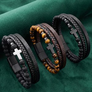 Peut inclure: Trois bracelets multicouches composés de cordons en cuir tressé, de perles en pierre lisses ou texturées et d'une breloque en forme de croix. Chaque bracelet possède un fermoir magnétique noir et associe des lanières en cuir à des perles.