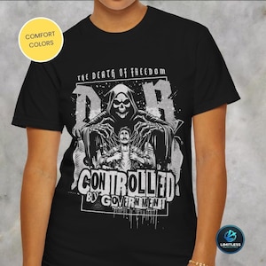 Puede incluir: Camiseta negra con un diseño gráfico que presenta una figura de la muerte y el texto "THE DEATH OF FREEDOM" y "CONTROLLED BY GOVERNMENT". El diseño es en tonos grises y blancos.