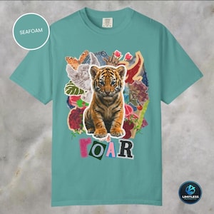 May include: Seafoam green t-shirt with a tiger cub graphic. The design includes a collage of flowers, butterflies, and the word "ROAR" in colourful letters. The shirt is a Comfort Colors brand.