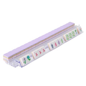May include: A complete Mahjong set with lavender tiles and a clear plastic rack. The tiles are arranged in rows, displaying various symbols and characters. The set includes tiles with floral and geometric designs, perfect for game night.