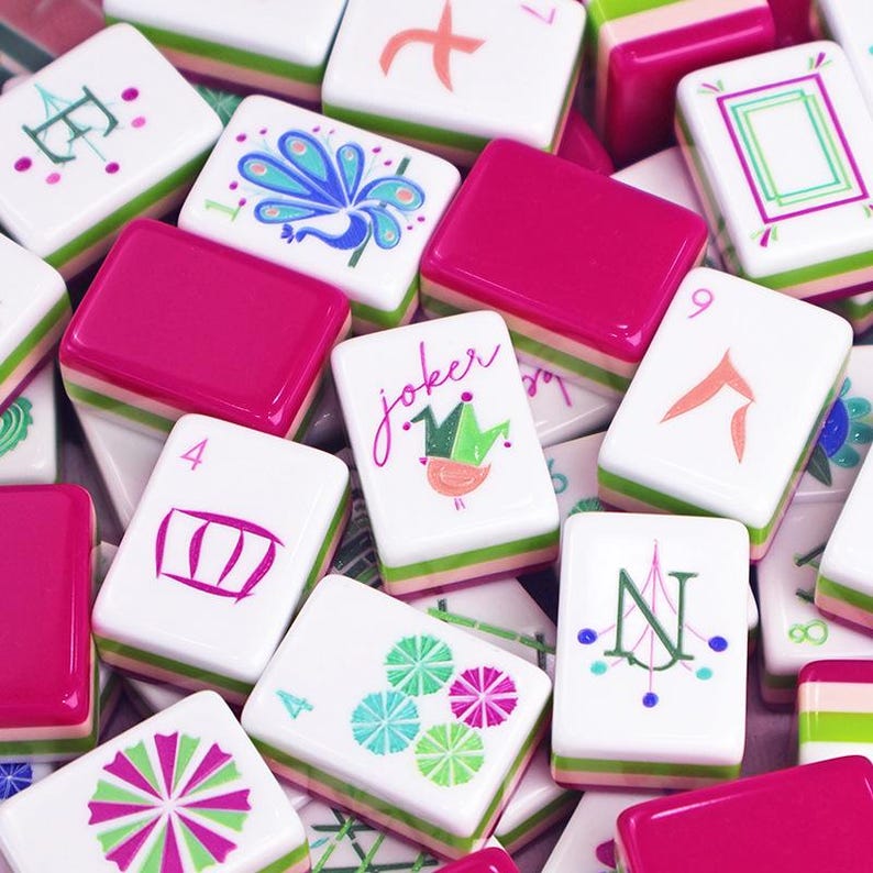 Puede incluir: Una colecci&oacute;n de coloridas fichas de Mahjong. Las fichas presentan varios dise&ntilde;os, incluyendo un pavo real, patrones florales y la palabra "Joker". Las fichas tienen una base blanca con acentos rosas y verdes.