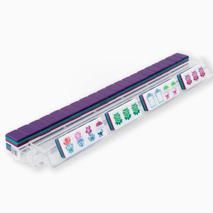 May include: A clear plastic tray holds a set of purple, teal, and white Mahjong tiles. The tiles are arranged in rows, with the purple tiles forming the majority. Some tiles have colorful floral and character designs.