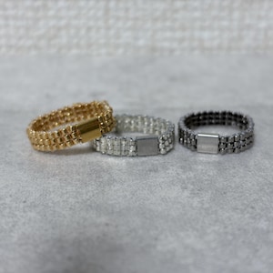 以下が含まれることがあります： 黒いハンドルと「But First, Coffee」のテキストが黒い太字で書かれた白いセラミックマグ。マグカップはぼやけた背景に置かれており、居心地の良い環境を示唆しています。