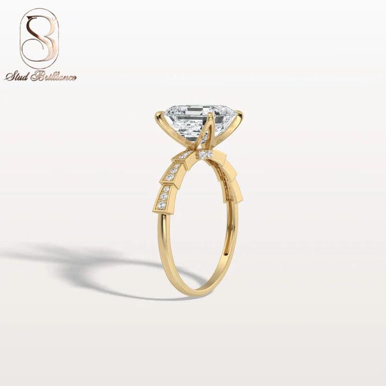 K&ouml;nnte beinhalten: Ein Goldring mit einem gro&szlig;en, im Smaragdschliff facettierten Mittelstein, der von vier Krappen gehalten wird. Die Ringschiene zeigt ein gestuftes, geometrisches Motiv mit kleinen Pav&eacute;-Diamanten an den Schultern und einer glatten Schiene.