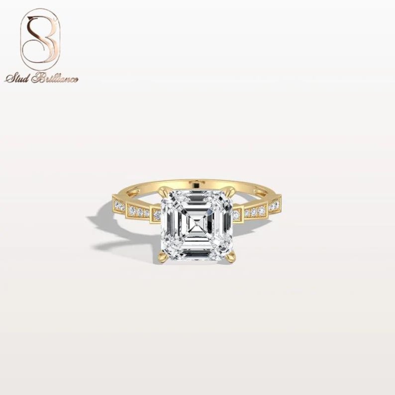 May include: A gold ring featuring a large, square-cut center stone with a step-cut facet pattern. The band is crafted from yellow gold and is accented with small, round, clear stones set along the shoulders on both sides of the center setting.