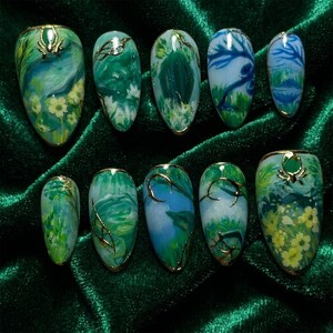 May include: A collection of ten artificial nails, each with a unique nature-themed design. The nails display green and blue landscapes with gold detailing. Some feature floral elements, while others have abstract patterns.