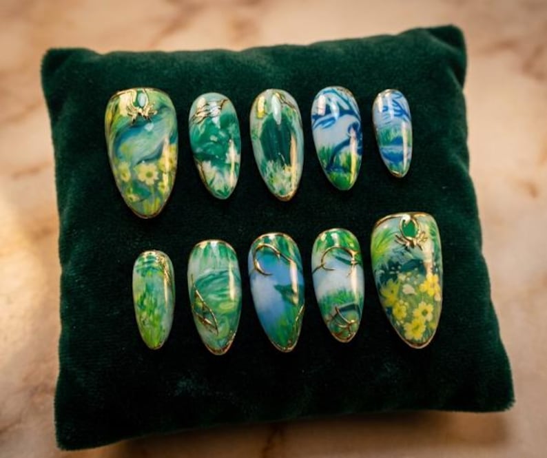 May include: A set of ten artificial nails with a nature-inspired design. Each nail features a base of green, blue, and yellow hues, with gold accents. The nails are arranged on a dark green velvet surface.