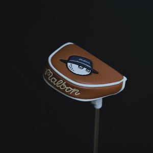 Puede incluir: Una taza de cerámica blanca con asa negra y el texto "But First, Coffee" en negrita negra. La taza se encuentra sobre un fondo borroso, sugiriendo un ambiente acogedor.