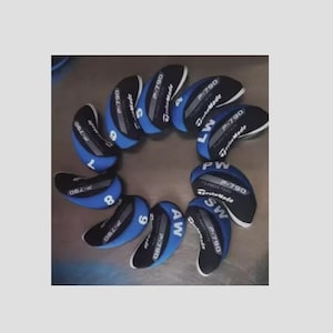 以下が含まれることがあります： 黒と青のゴルフヘッドカバーのコレクションが円形に配置されています。各カバーには「P-790」と「TaylorMade」の文字が印刷されており、「6」、「7」、「8」、「9」、「AW」、「SW」、「PW」、「LW」などのクラブ指定があります。