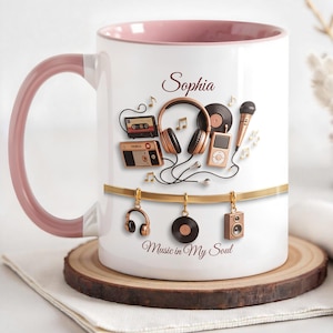 May include: White ceramic mug with a pink handle and interior. The mug is decorated with musical elements, including headphones, a cassette tape, and a microphone. The name "Sophia" is written on the mug, along with the phrase "Music in My Soul."