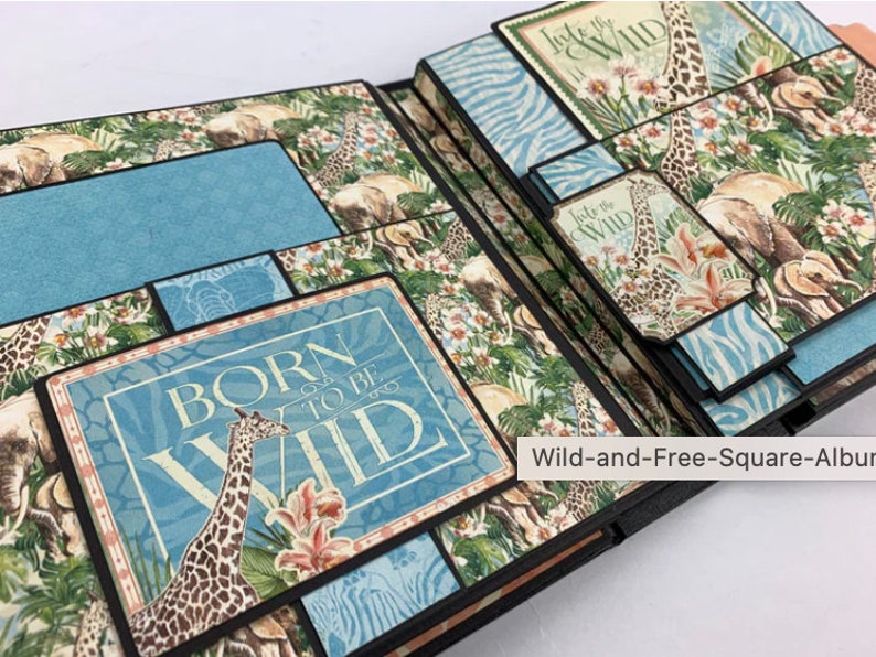 Puede incluir: &Aacute;lbum de recortes abierto con tem&aacute;tica de safari. Las p&aacute;ginas presentan ilustraciones de jirafas y elefantes, con detalles en azul y el texto "BORN TO BE WILD". El &aacute;lbum est&aacute; dise&ntilde;ado con p&aacute;ginas superpuestas y elementos decorativos.