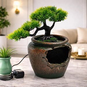 May include: A decorative bonsai tree in a weathered, brown ceramic pot with a large opening. The tree has vibrant green foliage and a dark, twisted trunk. A small green plant in a matching pot sits nearby.