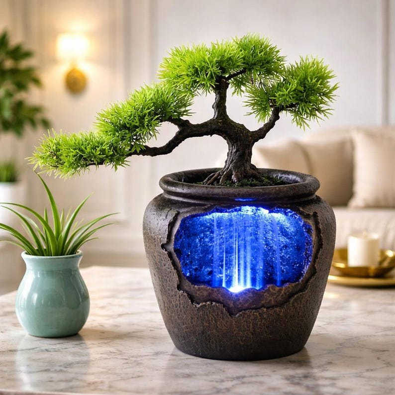 May include: A decorative bonsai tree in a textured brown pot with a blue waterfall effect. The bonsai has vibrant green foliage and a dark brown trunk. A small green plant in a light blue vase sits to the left.