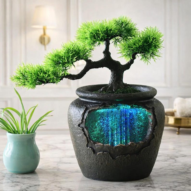May include: A decorative bonsai tree in a dark gray pot with a waterfall effect. The bonsai has vibrant green foliage and a dark trunk. The pot has a rectangular opening that reveals a blue and green waterfall feature.