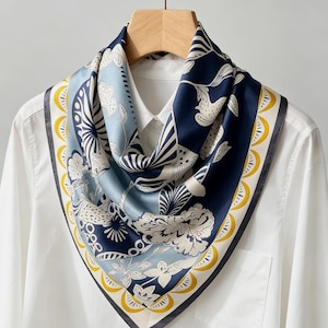 May include: A square silk scarf with a floral and abstract design. The scarf features a navy blue, light blue, and white color palette with a yellow border. The scarf is draped over a white collared shirt.