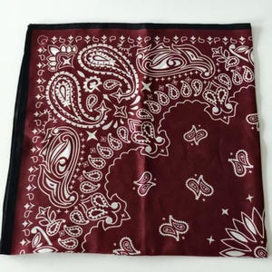May include: A square bandana featuring a deep burgundy background with a white paisley pattern. The design includes intricate teardrop-shaped motifs, floral elements, and small star shapes. The fabric has a smooth finish and a black border.