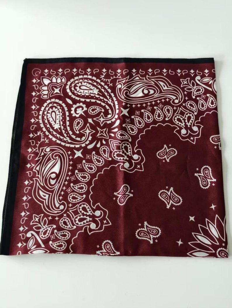 May include: A square bandana featuring a deep burgundy background with a white paisley pattern. The design includes intricate teardrop-shaped motifs, floral elements, and small star shapes. The fabric has a smooth finish and a black border.