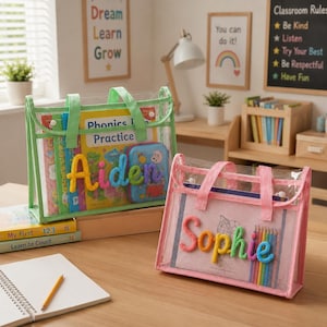 May include: Two rectangular clear plastic tote bags with fabric handles and trim. One bag is light green with the name Aiden in colorful yarn letters, containing books. The other is light pink with the name Sophie in yarn letters, containing paper.