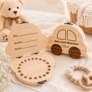 Puede incluir: Una caja de recuerdos de madera clara con forma de coche, con una tapa abatible que incluye el texto grabado Name, Date of birth y Blood type. La tapa exterior muestra el texto Baby teeth Memories y el nombre Noah con ruedas de madera oscura.
