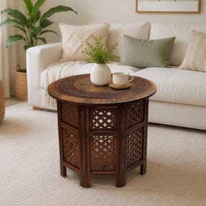 May include: A round, dark brown wooden side table featuring intricate hand-carved lattice patterns on its sides and a circular top with detailed floral carvings and small brass inlay accents. The table stands on a sturdy, multi-sided base.