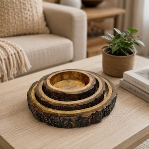 Könnte beinhalten: Ein Set aus drei ineinander verschachtelten runden Holzschalen mit natürlichem Rindenrand und einer glatten, goldbraun polierten Innenseite. Die Schalen sind konzentrisch gestapelt und zeigen die raue, dunkelbraune Textur der Baumrinde außen.