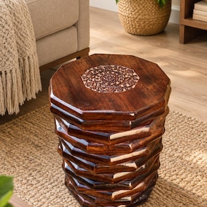 May include: A dark brown wooden stool with an octagonal shape and a tiered, stacked design. The top surface features a circular, intricate floral carving in the center, while the sides exhibit a smooth, polished finish with geometric edges.