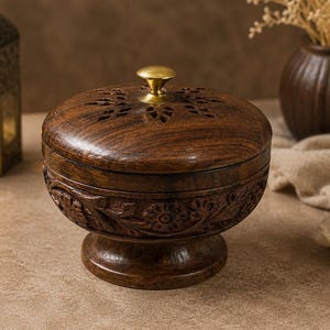 May include: A dark brown wooden bowl with a matching lid featuring intricate floral carvings on the sides and a star-shaped cutout pattern on the top. The lid is topped with a small, polished brass knob, and the bowl rests on a sturdy pedestal base.