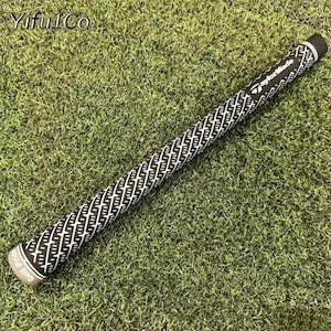 Puede incluir: Un grip de palo de golf en blanco y negro con un patr&oacute;n geom&eacute;trico repetitivo. El grip tiene el texto "TaylorMade" y "Golf Pride" impreso. El grip est&aacute; sobre un lecho de hierba verde.