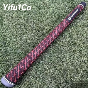 Puede incluir: Un grip de palo de golf con un patr&oacute;n geom&eacute;trico negro y rojo. El grip tiene una tapa gris con rayas blancas y el logotipo de TaylorMade. El grip est&aacute; sobre una superficie verde.
