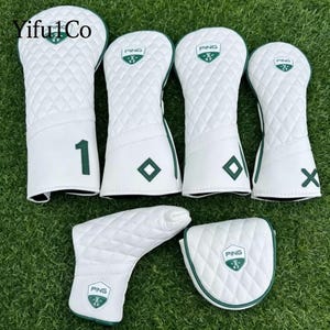 May include: A set of white golf club head covers with a quilted pattern and green accents. The covers feature the "PING" logo and a green number "1" and a green "X". The set includes covers for various club types.