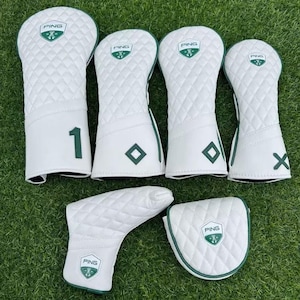 Puede incluir: Un conjunto de fundas para palos de golf blancas con un diseño acolchado y detalles en verde. Las fundas presentan el logotipo "PING" y varias marcas, incluyendo el número "1" y la letra "X".