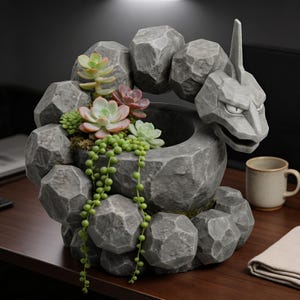May include: A gray, stone-like planter shaped like a Pokémon character, featuring a round opening for plants. The planter is filled with various succulents and trailing plants. A mug and folded cloth are on the wooden surface.