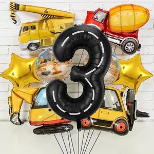 Puede incluir: Una colección de globos coloridos con temática de construcción. Incluye un gran globo negro con el número 3 con marcas viales blancas, globos amarillos en forma de estrella y varios globos con forma de vehículo.