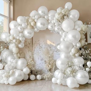 May include: A white balloon arch decorated with various sizes of white balloons and white flowers. The arch is set against a neutral background, creating a soft and elegant display. Perfect for weddings, parties, or other special events.