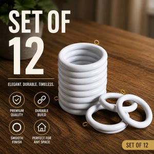 Pode incluir: Um conjunto de 12 argolas de cortina brancas com pequenos ilhós de metal dourado. As argolas estão empilhadas verticalmente numa coluna, com duas argolas adicionais deitadas à frente. O texto "SET OF 12" e "ELEGANT. DURABLE. TIMELESS." é visível.