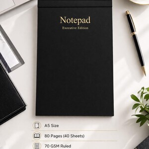 Könnte beinhalten: Ein schwarzes Notizbuch im A5-Format mit goldfarbenem Schriftzug "Notepad Executive Edition". Es hat 80 Seiten, 70 g/m² liniertem Papier und einen 300 g/m² weichen, matt laminierten Umschlag. Der Text "Clean pages. Clear thoughts. Better every day." steht unten.