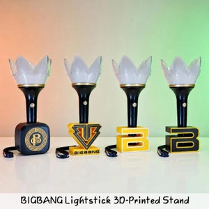 May include: Four black and white lightsticks with crown-shaped tops, each mounted on a unique 3D-printed stand. The stands feature distinct designs including a circular logo, a geometric emblem, and the letter B in yellow and black color schemes.