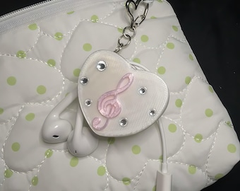 May include: A white heart-shaped earphone cable tidy featuring a light pink treble clef emblem, five small clear rhinestones, and a silver-toned heart-shaped keyring attachment. The device is shown with white wired earphones and a USB-C connector.
