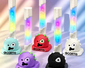 Könnte beinhalten: Eine Sammlung von CORTIS-Leuchtstäben, jeder mit einem 3D-gedruckten Sockel in Form eines Cartoon-Monsters in verschiedenen Farben wie Hellblau, Rot, Lila, Schwarz und Weiß, mit dem Text CORTIS auf dem Sockel.