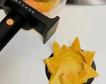 Könnte beinhalten: Ein schwarzer Leuchtstab mit dem in Weiß gedruckten Text TAFYANG und einem runden orangefarbenen Leuchtelement. Daneben befindet sich ein runder schwarzer Sockel mit einem gelben, sternförmigen Ständer mit texturiertem, zahnradartigem Design.