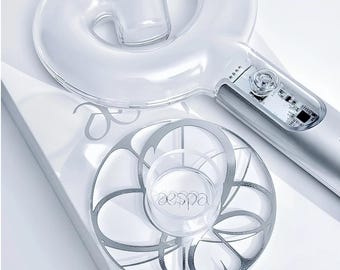 Könnte beinhalten: Ein transparenter Acryl-Lightstick-Ständer mit einer kreisförmigen Basis, einem silbernen, blumenartigen Muster und dem mittig aufgedruckten Text aespa. Der Ständer ist für einen transparenten, spiralförmigen Lightstick mit sichtbarer Elektronik.