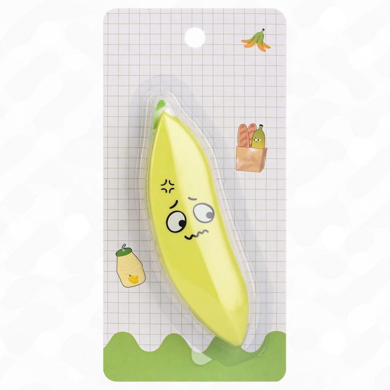 May include: A yellow banana-shaped eraser with a cartoon face, packaged in clear plastic. The eraser has a green tip and is set against a white grid background with small illustrations of a banana peel, bread, and a jar.
