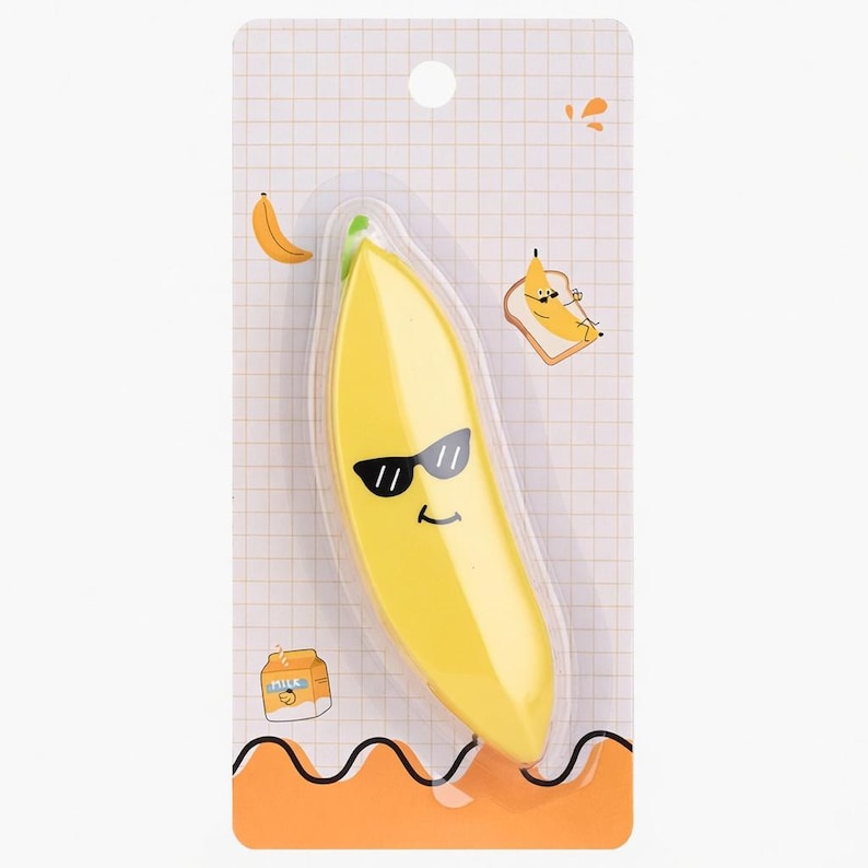 May include: A yellow banana-shaped eraser with black sunglasses and a smiling face, packaged on a white and orange card. The card features cartoon illustrations of a banana, toast, and a milk carton.