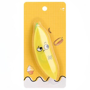 May include: A yellow banana-shaped pencil sharpener with a cartoon face and a bandage sticker, packaged on a yellow grid-patterned card. The card features illustrations of a banana, hot dog, and ice cream cone.