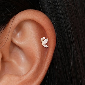 May include: A small gold-toned earring shaped like a butterfly with clear, sparkling stones set into the wings. The piece is positioned in the upper cartilage area of the ear, featuring a delicate metal frame and a secure post backing design.