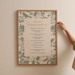May include: A framed wall art print featuring the text The Ten Commandments in gold lettering, surrounded by a botanical border of sage green birds, leaves, and flowers on a cream background. The print is enclosed in a simple light wood frame.