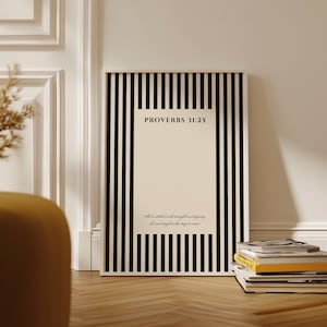 May include: A rectangular wall art print featuring a vertical black and white striped border surrounding a cream-colored center. The text reads PROVERBS 31:25 followed by the script phrase She is clothed with strength and dignity; she can laugh at the days to come.