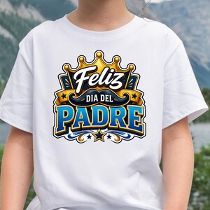 May include: White t-shirt featuring a colorful graphic design. The design includes the words "Feliz Dia Del Padre" in blue and gold, with a crown and mustache. The shirt is suitable for Father's Day.