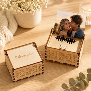 Könnte beinhalten: Zwei hölzerne Spieluhren mit floralen Mustern. Auf einer Schatulle steht der Text "I love you" eingraviert. Die andere Schatulle zeigt ein Foto eines Paares und ein Schallwellenmuster. Die Schatullen sind geöffnet und geben den Blick ins Innere frei.