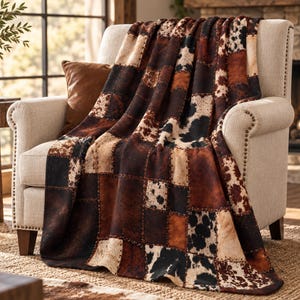 Puede incluir: Una manta con un diseño de patchwork que presenta varios patrones de piel de vaca en tonos marrón, negro y crema. La manta está colocada sobre un sillón tapizado, mostrando una cuadrícula repetitiva de texturas animales.